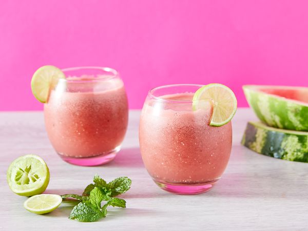 Deux verres de smoothie à la pastèque, avec du citron vert et de la menthe, sur fond rose.