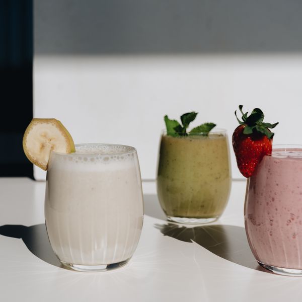 Trois smoothies aux teintes crème, verte et rose, garnis de fruits.